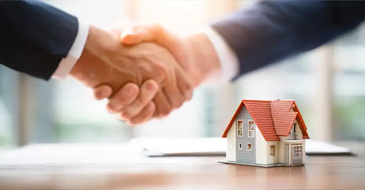 Händedruck zwischen zwei Personen neben einem Modellhaus